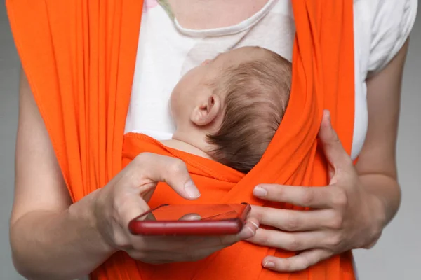 Обрезание матери с ребенком в стропе, держа смартфон — стоковое фото