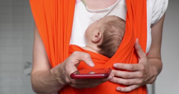 Madre de la cosecha con el bebé en la honda celebración de teléfono inteligente — Vídeos de Stock