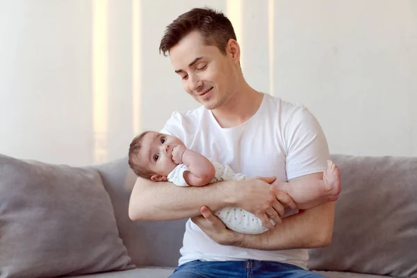Młody ojciec siedzi na kanapie i trzymając dziecko na ręce — Zdjęcie stockowe
