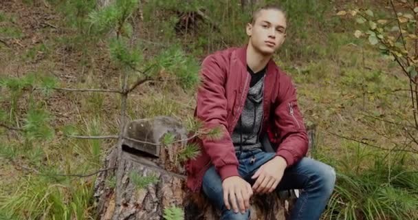 Ontspannen jongeman zittend op boomstronk — Stockvideo