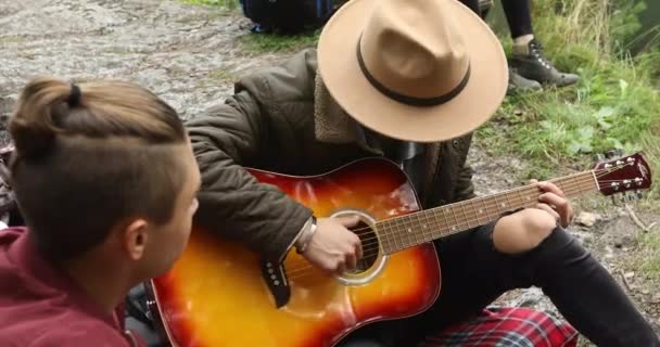 Hombres jóvenes sentados en el suelo y tocando la guitarra — Vídeos de Stock