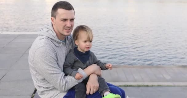 Jeune homme assis sur la jetée avec bébé — Video