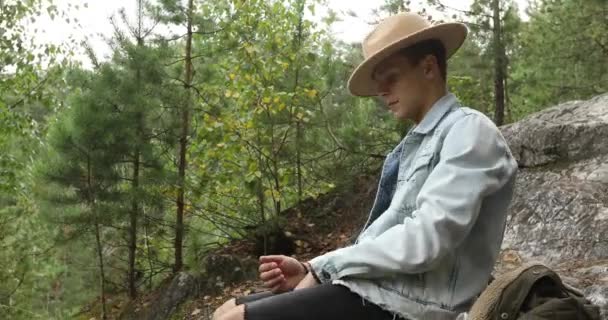 Mladý muž sedí na skále v lese — Stock video