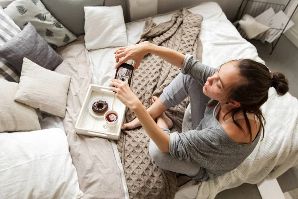 Kvinnan tar skott av bricka med mat på sängen — Stockfoto