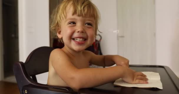 Niño alegre se sienta en silla de niños y se ríe — Vídeos de Stock