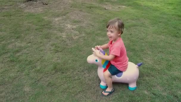 Lindo poco rubia chico cabalgando en caballo juguete unicornio — Vídeo de stock