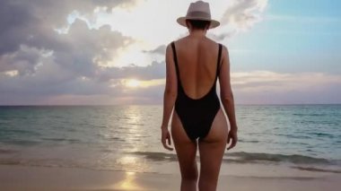 Kadın deniz gün batımına doğru yürüyor