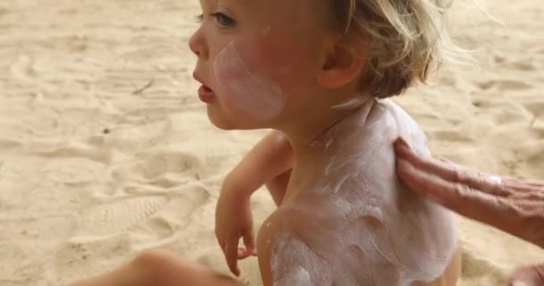 Moeder zonnebrand lotion toe te passen op zoon terug op het strand — Stockvideo