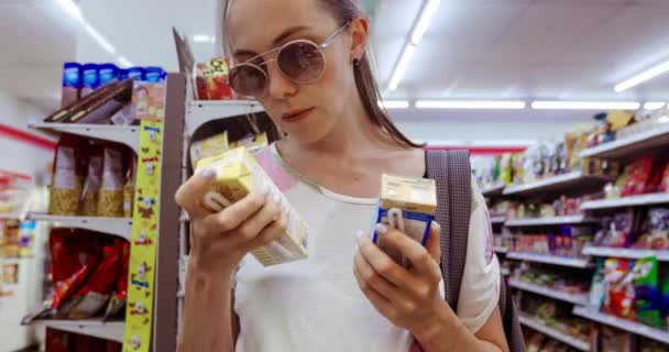 Молодая женщина выбирает между двумя коробками в магазине — стоковое видео