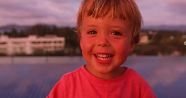 Маленький хлопчик дивиться на камеру під час заходу сонця — стокове відео