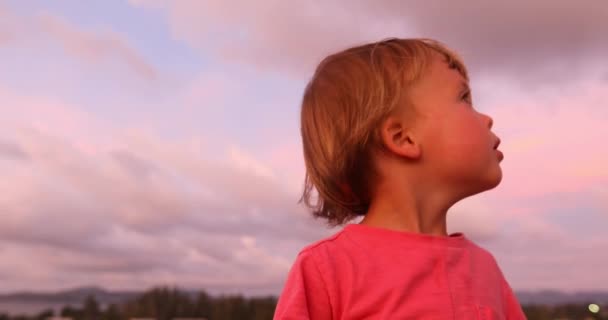 Encantador niño en la puesta de sol mirando a su alrededor — Vídeos de Stock