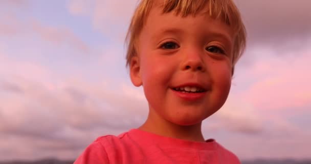 Liten pojke tittar på kameran i solnedgången — Stockvideo