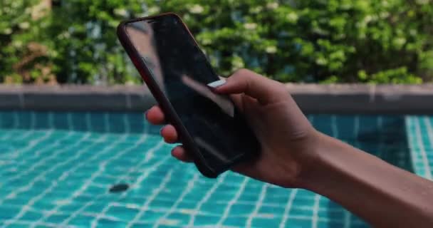 Crop hand using smartphone near swimming pool — Stock Video