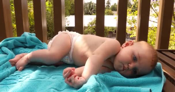 庭の木製ベビーベッドの中青いタオルの上に横になっているおむつの甘い小さな赤ちゃん — ストック動画