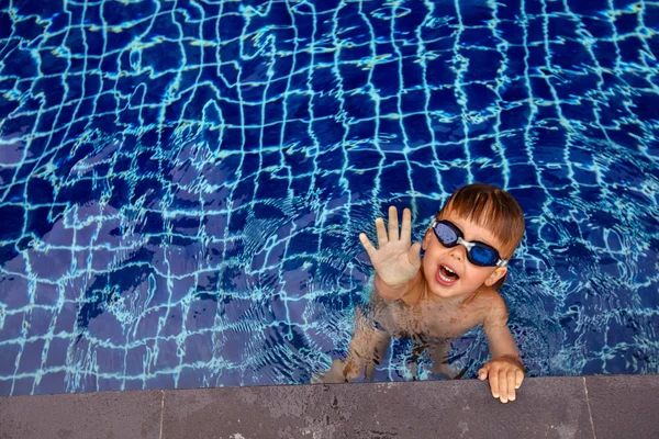 Funny boy in swimming pool reaching out camera