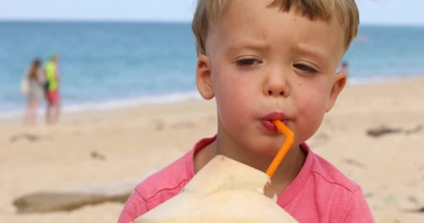 Lindo niño bebiendo agua de coco en la playa — Vídeo de stock