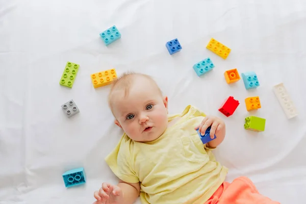 Lilla barnet ligger på vitt linne mellan leksaker — Stockfoto