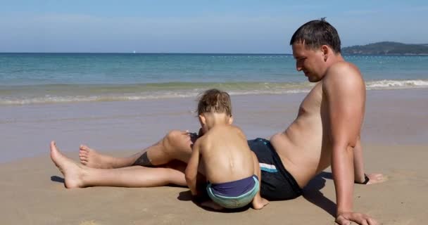 Мальчик играет рядом с отцом на пляже — стоковое видео