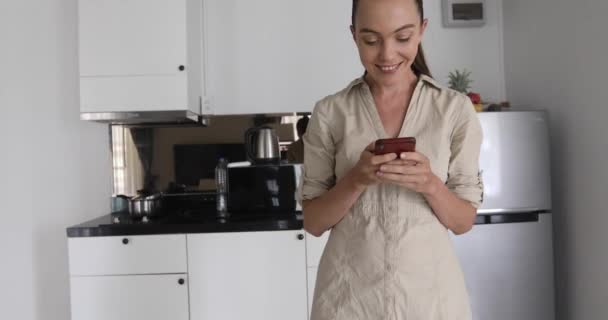 Smiling female using smartphone in kitchen — Stock Video