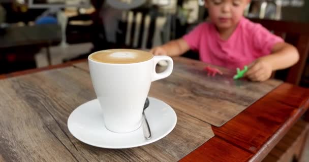 Child plays toys next to mug cappuccino — Stock Video