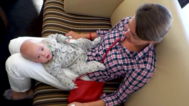 Žena s dítětem na klíně sedí na pohovce — Stock video