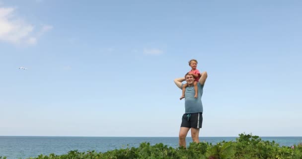 L'uomo tiene sulle spalle suo figlio sfondo mare — Video Stock