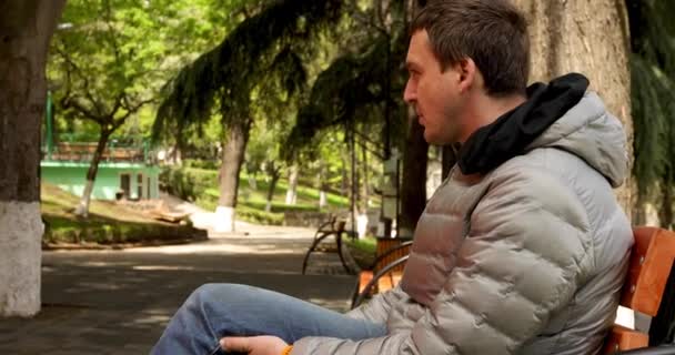 Homem senta-se em um banco no parque na primavera — Vídeo de Stock