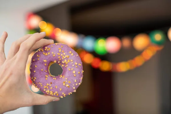 Person holding glazed donut against street garland — Stock Photo, Image