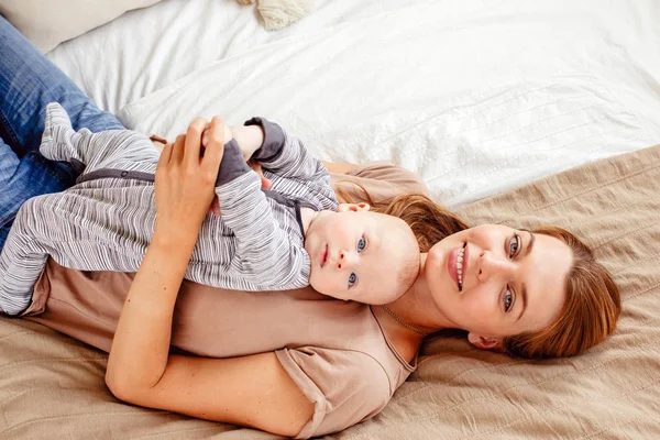 Улыбающаяся мать с ребенком, лежащим на кровати — стоковое фото