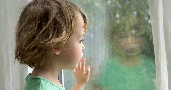 Junge steht und schaut aus dem Fenster — Stockfoto