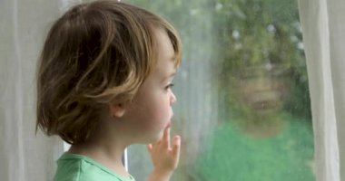 Çocuk ayakta ve pencereden dışarı bakıyor