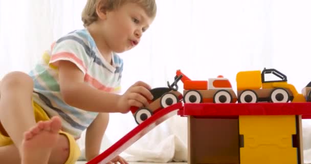 Niño de tres años juega con coches de juguete de madera — Vídeo de stock