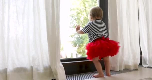 Linda niña descalza en falda roja mirando a la ventana — Vídeos de Stock