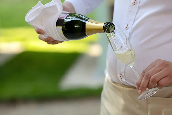 Waiter pouring champagne into glass with thin leg — Stock Photo, Image