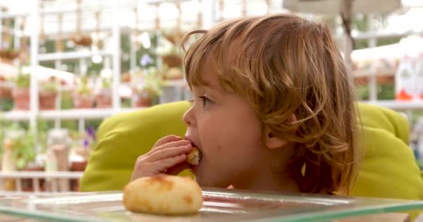 Задумчивый ребенок ест булочку за столом в кафе — стоковое видео