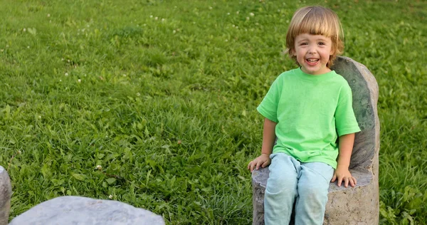 Niño sentado en la silla de piedra en el parque — Foto de Stock