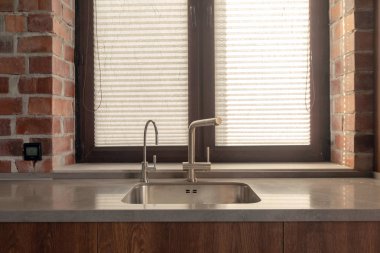 Pencere ve tuğla duvar yanında birkaç musluk ile Mutfak lavabo