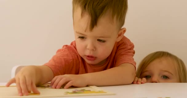 Годовалый ребенок смотрит, как трехлетний ребенок играет с головоломкой — стоковое видео