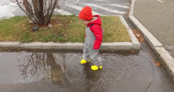 Jongen met gele laarzen die door plassen loopt — Stockvideo