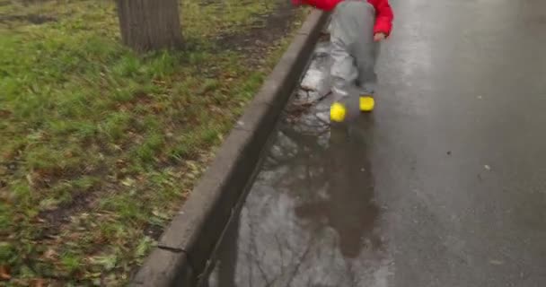 Niño con botas amarillas corriendo a través de charcos — Vídeos de Stock