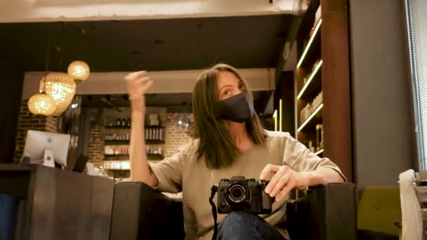 Mujer en máscara facial con cámara fotográfica digital delante del espejo en el salón — Vídeos de Stock