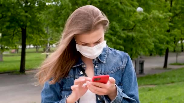 Poważna kobieta w masce medycznej za pomocą smartfona w parku — Wideo stockowe
