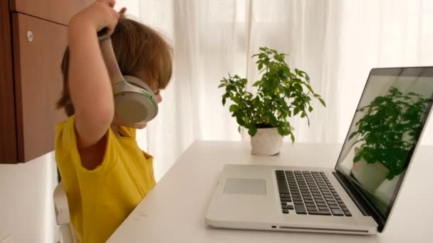Малюк одягає навушники перед ноутбуком — стокове відео