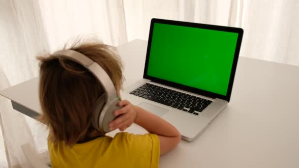 Barn i hörlurar framför en grön bärbar skärm — Stockvideo