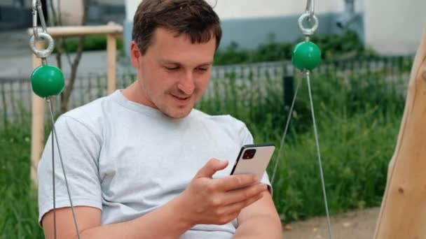 Jeune homme utilisant un smartphone sur une aire de jeux — Video