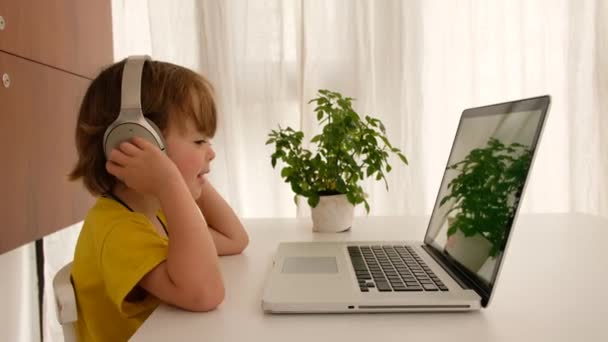 El niño escucha música en los auriculares delante de la computadora portátil — Vídeo de stock