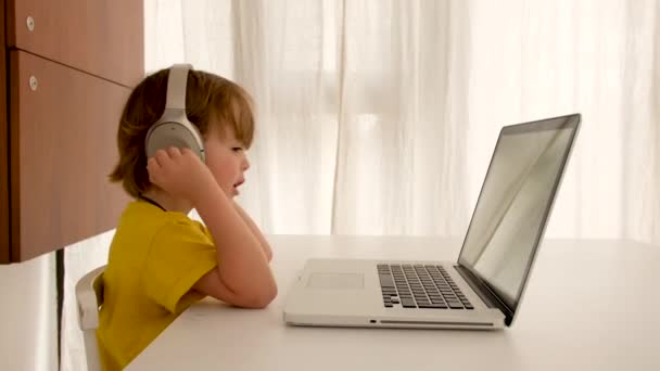 El niño escucha música en los auriculares delante de la computadora portátil — Vídeos de Stock