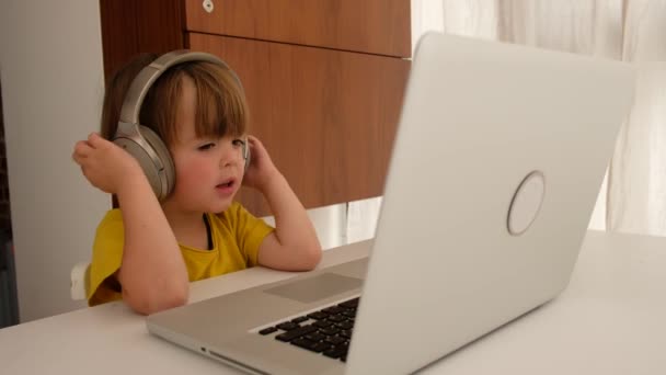 El niño escucha música en los auriculares delante de la computadora portátil — Vídeos de Stock