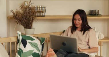 Evdeki koltukta dizüstü bilgisayarı olan bir kadın kameraya bakıyor.