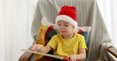Kırmızı Noel şapkalı küçük çocuk turuncu kitap kapağı okuyor.